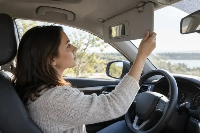 An adult driver checking a sun visor in a parked unbranded car in daylight.