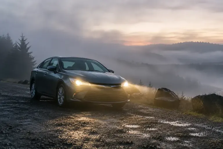 Parked car in mist with normal headlights visible.