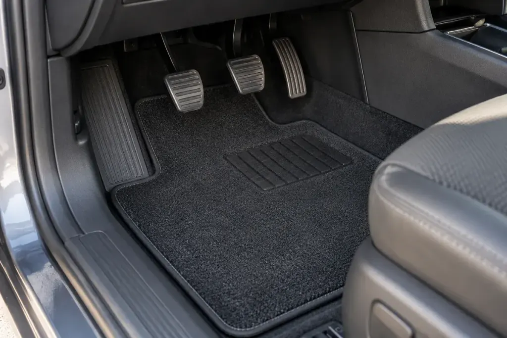 Clean car driver footwell with a fitted floor mat and unobstructed pedals, parked vehicle.
