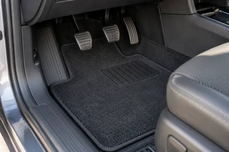Clean car driver footwell with a fitted floor mat and unobstructed pedals, parked vehicle.