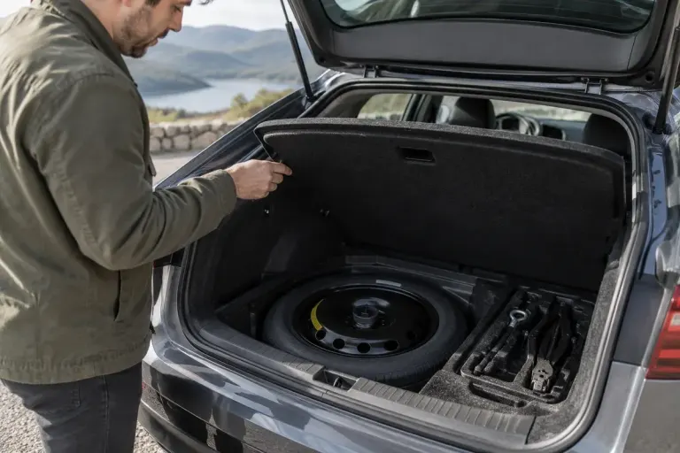 An open car boot showing a secured compact spare wheel and neatly stored wheel tools.